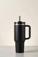 Black Stanley tumbler with handle and straw on a light background